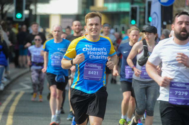 A group of people running together in Sheffield Half Marathon. One runner wears a Children's Hospital Charity shirt.